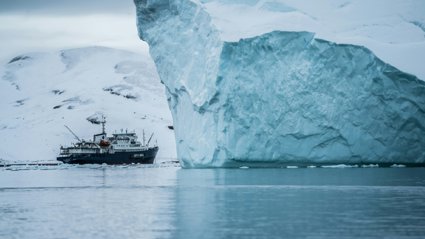 Iceberg with a ship sailing closely next to it.