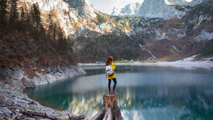 Person standing on broken tree trunk overlooking a lake and mountains.