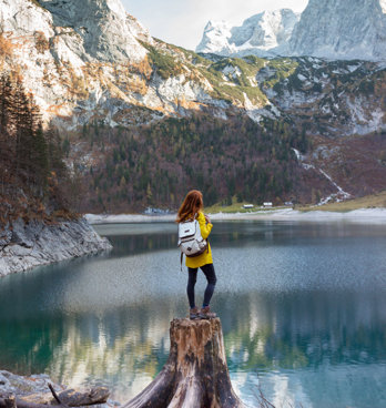 Person standing on broken tree trunk overlooking a lake and mountains.