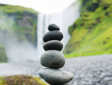Selective focus of a stack of rocks balanced in front of waterfall.