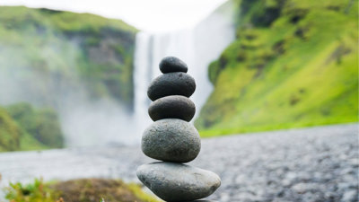 Selective focus of a stack of rocks balanced in front of waterfall.