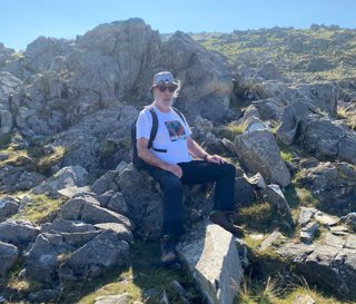 Des Bowden sitting on top of a grassy rock formation.
