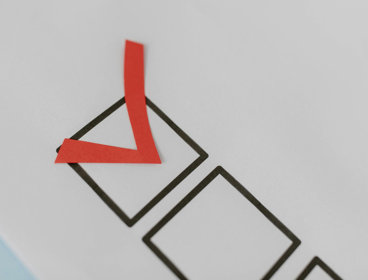 Red paper tick placed inside a black checkbox on a white sheet of paper.