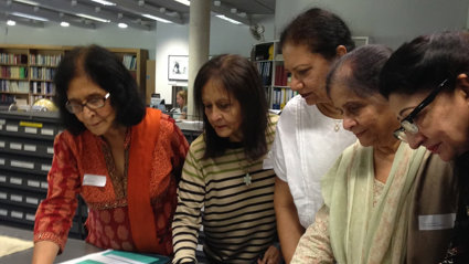 Five people looking at material displayed on a table in a library.