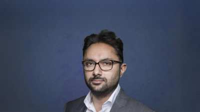 Person with glasses against dark blue background.