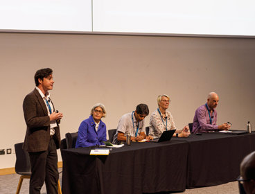 Panellists on stage at the annual conference in 2025 in Birmingham. There are four people seated and one standing