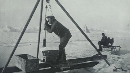 Old black and white photo of a person using scientific equipment in a polar environment.