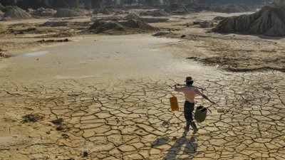 Person carrying water over dry lake with cracked earth.
