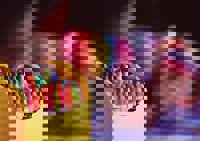A box of coloured crayons with a blurred image of a child using them in the background