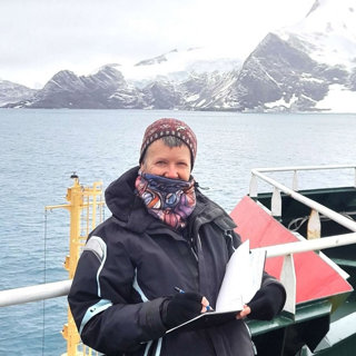 Claudia Myatt sketching while on a boat with snow mountains behind
