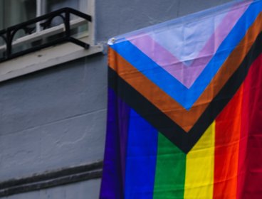 The LGBTQ+ flag hanging outside a window. 