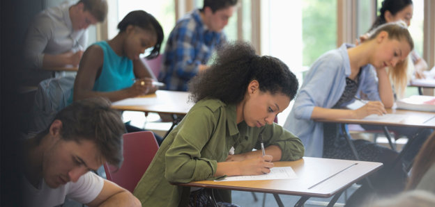 Students sitting at desks in a classroom, focused on writing during an exam.
