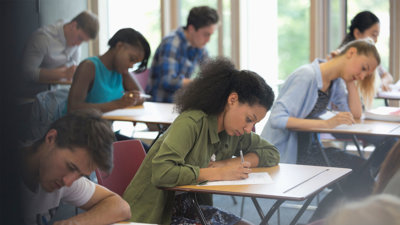 Students sitting at desks in a classroom, focused on writing during an exam.