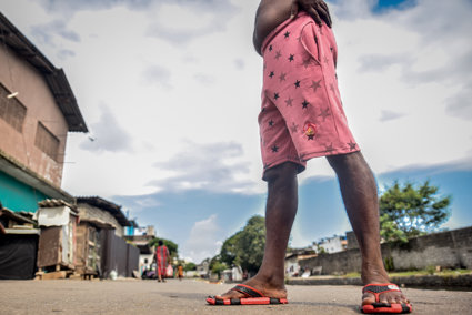 A pair of flip flopped feet, standing ona road with settlements behind