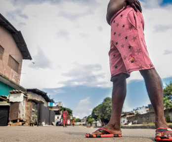 A pair of flip flopped feet, standing ona  road with settlements behind