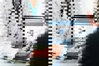A doctor sits opposite a patient and shows them an infomation page of their laptop